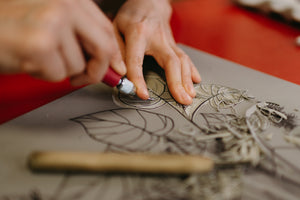 A close up of Julie Wall's hands as she carves a linoleum block by hand in her studio. 